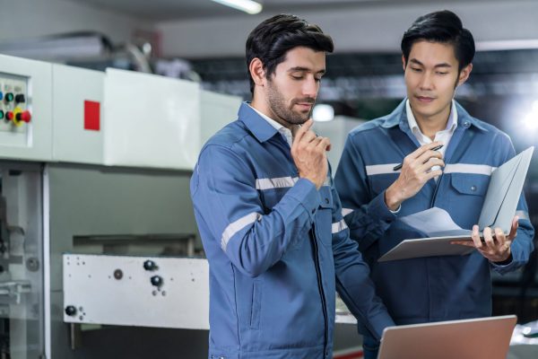 Male Asian caucasian engineer professional having a discussion standing consult at machine in the factory ,two expert coworker brainstorm explaining and solves the process of the cnc operate machine