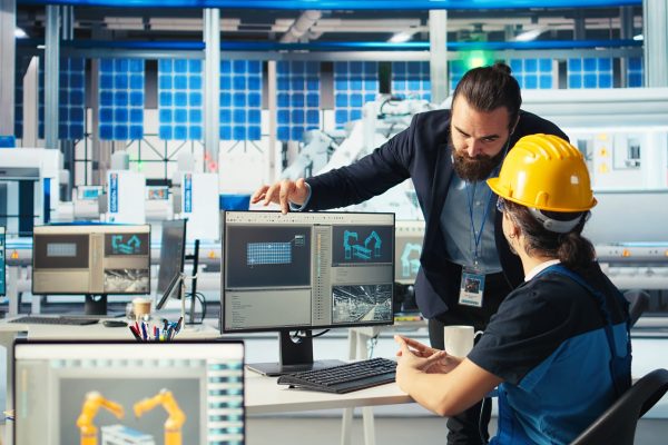 Solar panel manufacturing plant manager showing engineer on PC how to develop prototypes for new solar energy systems. Team leader telling technician about new photovoltaics materials, camera A