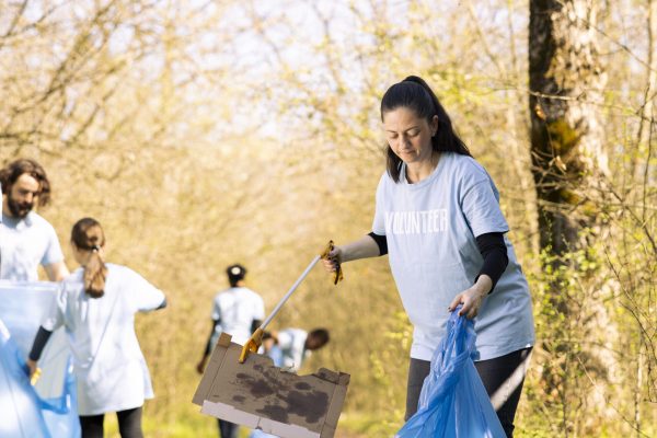 Woman environmentalist grabbing rubbish with a claw tool in the woods, clearing ecosystem of trash and plastic junk. Female activist doing voluntary work to tidy up the forest area.